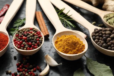 Siyah masadaki kaşıklardaki farklı baharatlar, yakın plan.