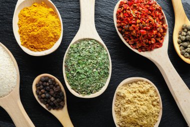 Siyah masada kaşıklardaki farklı aromatik baharatlar, yakın plan.