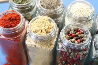 Mavi arka planda kavanozlardaki farklı aromatik baharatlar, yakın plan.