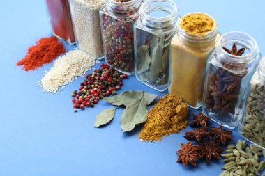 Mavi arka planda kavanozlardaki farklı aromatik baharatlar, yakın plan.