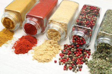 Beyaz masadaki kavanozlarda farklı aromatik baharatlar, yakın plan.