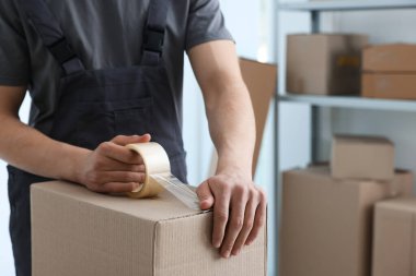 Kapalı alanda yapıştırıcı bantlı karton kutu mühürleyen adam.