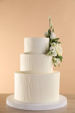Ahşap masada bej arka planda çiçeklerle süslenmiş nefis düğün pastası, yakın plan.