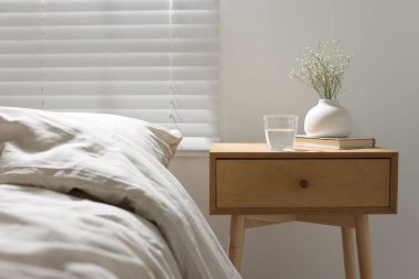 Komodinin yanında vazoda çiçekler, bir bardak su ve yatağın yanında kitap.