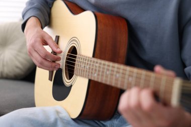 Genç adam kanepede gitar çalıyor, yakın plan.