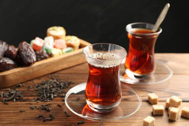 Cam bardaklarda geleneksel Türk çayı, kuru yapraklar, kahverengi şeker ve tatlılar ahşap masada, yakın plan