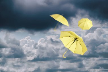 Bulutlu gökyüzünde uçan sarı şemsiyeler. Fırtınalı hava