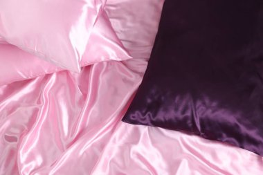 Lüks pembe ipek çarşaflar ve yastıklar yatağın üstünde.