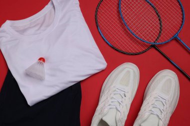 Spor kıyafetleri, spor ayakkabıları, badminton raketleri ve kırmızı arka planda mekik penisi, düz yatıyordu.