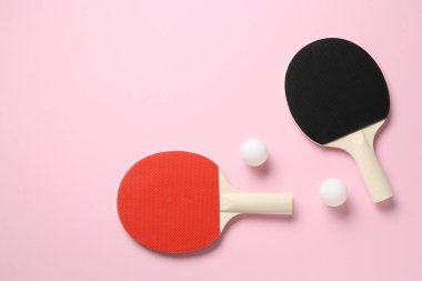 Masa tenisi raketleri ve pembe arka planda toplar, düz yatış. Metin için boşluk