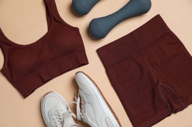 Spor kıyafetleri, halterler ve spor ayakkabıları bej arka planda, düz yatıyordu.