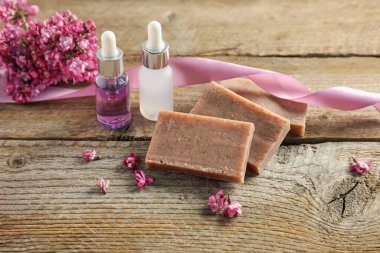 Sabun çubukları, temel yağ ve ahşap masadaki leylak çiçekleri.