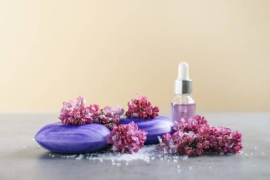 Sabun çubukları, deniz tuzu esaslı yağ ve leylak çiçekleri bej arka planda gri desenli masa, yakın plan