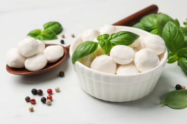 Lezzetli mozzarella peynir topları kasede, kaşıkta, fesleğende ve biberlikte beyaz mermer masada, yakın plan