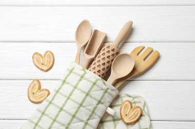 Fırın eldivenindeki farklı mutfak aletleri ve beyaz ahşap masada düz duran avuç içi kurabiyeler.