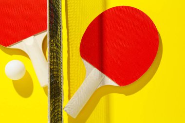 Ping pong raketleri, top ve ağ sarı arka planda, düz yatıyordu