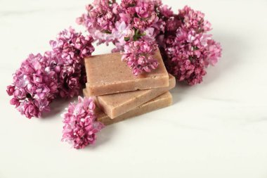 Beyaz masanın üzerinde sabun ve leylak çiçekleri yığını, yakın plan.