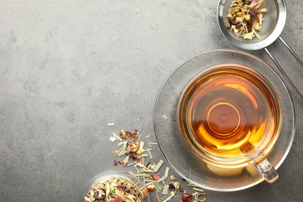 Aromatik bitki çayı ve kuru yapraklar gri masada, düz yerde. Metin için boşluk