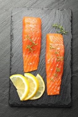 Deniz ürünleri. Somon fileto parçaları, kekik ve limon dilimleri siyah desenli masa, üst manzara.