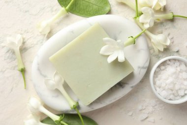 Bir kalıp sabun, deniz tuzu ve yasemin çiçekleri ışık masasında, düz yatıyordu.