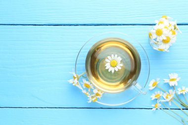 Cam fincanda nefis papatya çayı ve açık mavi ahşap masada taze çiçekler. Metin için boşluk