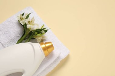Bir şişe yumuşatıcı, çiçekler ve bej arka planda terry havlular, düz yatak. Metin için boşluk