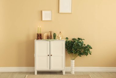 Havalı şamdanlar, yanan mumlar ve kapalı alandaki bej duvarın yanındaki dolaptaki diğer dekorlar.