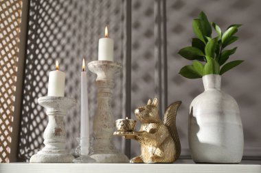 Zarif şamdanlar, yanan mumlar, vazoda dallar ve gri duvarın yanındaki şifoniyerde diğer dekorlar.