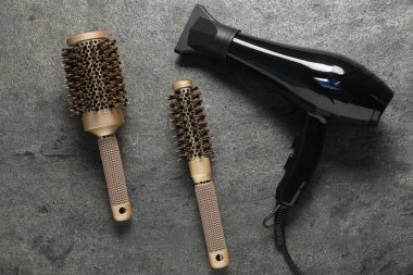 Gri desenli arka planda saç kurutma makinesi ve fırçalar.
