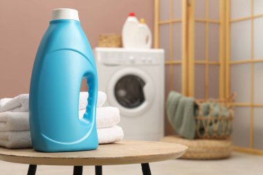 Bir şişe yumuşatıcı ve ahşap masa üzerinde havlular, metin için yer.