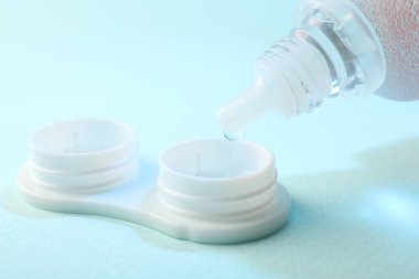 Açık mavi arkaplanda kontak lensleri olan çözelti dosyaya damlıyor, yakın plan