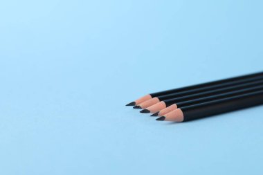 Açık mavi arka planda birçok keskin grafit kalem, yakın plan. Metin için boşluk