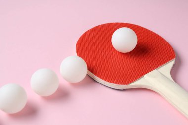 Pembe arka planda pinpon raketi ve toplar, yakın plan.