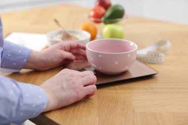 Mutfak terazisinde yulaf ezmesi tartan kadın, kapalı masa, yakın plan.