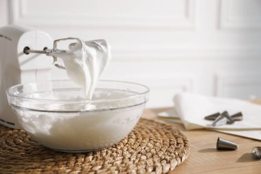 Kapalı masa üzerinde çırpılmış krema ve çırpılmış kremayla el çırpıcı, yakın plan.