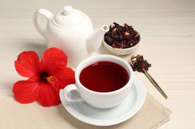 Lezzetli amber çayı fincanda, çaydanlıkta, kuru roselle sepals ve açık ahşap masada çiçek.