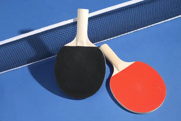 Masa tenisi raketleri ve mavi arkaplanda ağ.