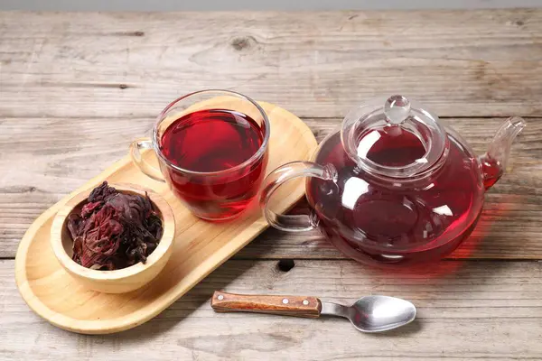Cam fincanda lezzetli amber çayı, çaydanlık, kuru roselle sepals ve tahta masada kaşık.
