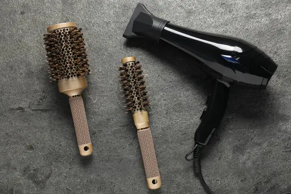 Gri desenli arka planda saç kurutma makinesi ve fırçalar.