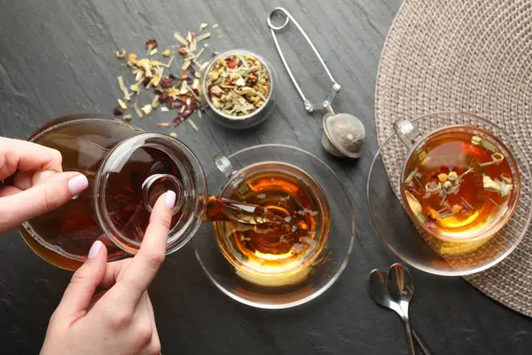 Siyah masada çaydanlıktan fincana bitki çayı döken kadın.