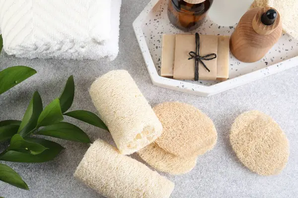 Açık gri masa üzerinde farklı lif süngerleri, havlular ve kozmetik ürünleri düz yatıyordu.