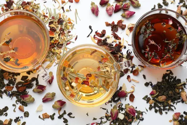 Beyaz arka planda farklı bitkisel çaylar ve kuru yapraklar.