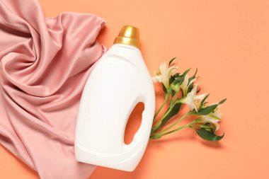 Bir şişe yumuşatıcı, çiçekler ve mercan zemin üzerinde pembe kumaş, düz uzanmış.