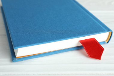 Beyaz ahşap masa üzerinde kırmızı kurdele yer imi olan kitap, yakın plan.