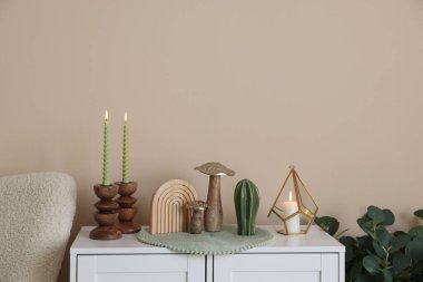 Havalı şamdanlar, yanan mumlar ve kapalı alandaki bej duvarın yanındaki dolaptaki diğer dekorlar.