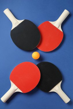 Masa tenisi raketleri ve top mavi arka planda, düz yatıyordu.
