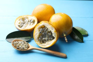 Olgun tutku meyveleri, yeşil yapraklar ve tohumlar açık mavi ahşap masada, yakın plan.