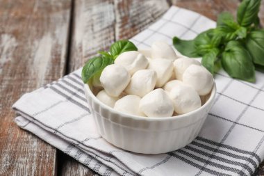 Lezzetli mozzarella peynir topları kasede ve fesleğen ahşap masada, yakın plan.