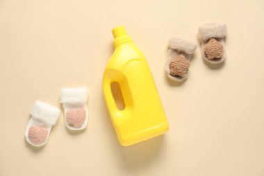 Bir şişe yumuşatıcı ve bej arka planda bebek çorapları.