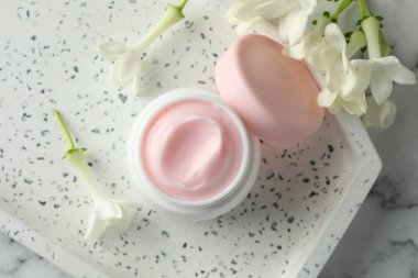 Bir kavanoz nemlendirici vücut kremi ve beyaz mermer masa üzerinde çiçekler, düz uzanmış.